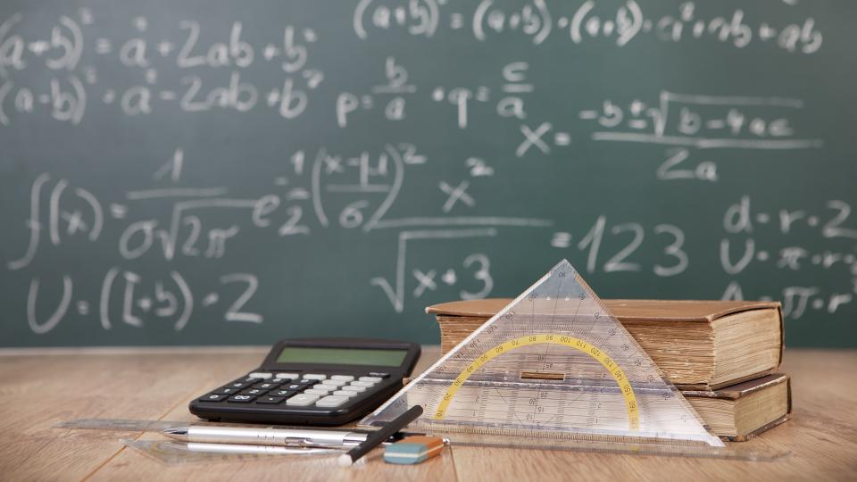Auf einem Schreibtisch sind zwei Lehrbücher, zwei Geodreiecke, drei Stifte, ein Radiergummi, ein Lineal und ein Taschenrechner abgebildet. Im Hintergrund befindet sich eine Schultafel, auf der mathematische Formeln stehen. 