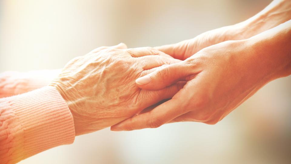 Eine ältere und eine jüngere Person halten sich an den Händen.