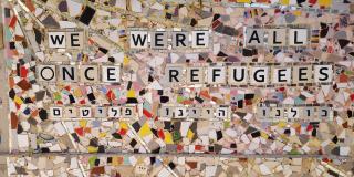 Ein Gemälde aus weißem und buntem Mosaikglas, auf dem "we were all once refugees" (zu Deutsch: Wir waren alle einmal Flüchtlinge) steht.