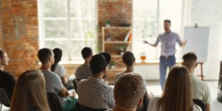 Ein männlicher Redner hält eine Präsentation vor einer Gruppe an Zuhörern in einer Universität