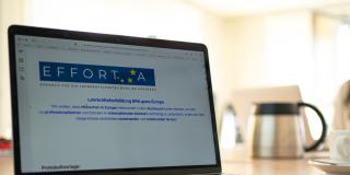 Abgebildet ist ein aufgeklappter Laptop. Auf dem Bildschirm sind das Logo zu Effort-A und die Aufschrift "Lehrkräftefortbildung BRA goes Europe" zu erkennen.