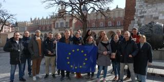 Abgebildet sind 26 Lehrkräfte der beruflichen Bildung, die vor einem imposanten Gebäude stehen und eine Flagge der EU hochhalten. 