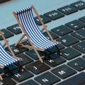 Zwei gestreifte Sonnenstühle stehen in Miniaturform auf einer beleuchteten grauen Tastatur von einem Laptop