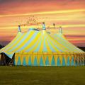 Ein blaugelbes Circus Zelt vor einem Sonnenuntergang auf einer Wiese