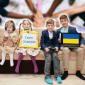 Vier Kinder sitzen auf einem Sofa. Ein junges Mädchen hält eine Tafel mit der Aufschrift "Learn Ukrainian" (zu Deutsch: Ukrainisch lernen) in ihren Händen. Auf dem Schoß eines Jungen befindet sich ein Laptop. Auf dem Bildschirm ist die Flagge der Ukraine abgebildet. In seiner rechten Hand hält er ein Buch. Die beiden anderen Kinder halten jeweils ein Handy in ihren Händen. 