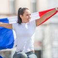 Eine junge Frau hält eine ausgebreitete Flagge Frankreichs hinter ihrem Rücken.