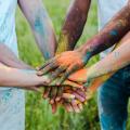 Eine Gruppe junger Menschen legt die mit bunter Kreide gefärbten Hände übereinander.